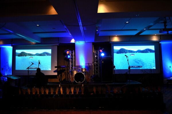 Two Projector screens and other audio visual equipment displayed at a corporate event. Projector screen hire from Auckland Event Hire Services Company The Rock Factory