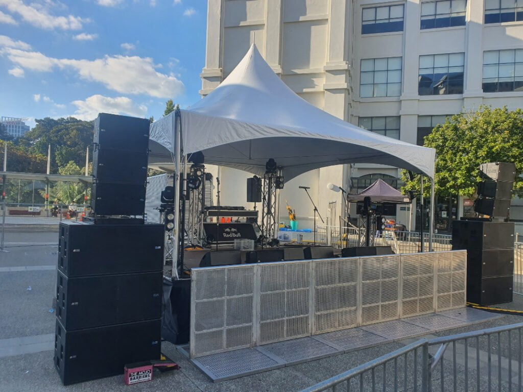 Photo shows a outdoor music festival production setup with covered stage with one of our sound systems set up either side of the stage