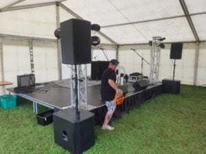 This photo shows the Basic PA hire package 2 being setup for a band and DJ in a tent on top of one of our stages for hire. Our Basic PA system Packages are great for all manner of events, anf for DJs and Bands who need something compact. The DJ PA System option 2 is often referred to as the subs poles tops system and is popular for events that want something powerful and symmetrical. 