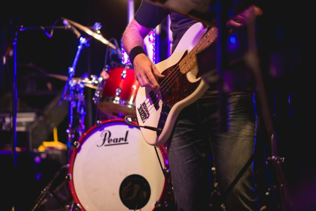 Photo of Live Band Auckland. It shows the bassist infront of the drum kit playing live onstage. Book live entertainment at your next event.