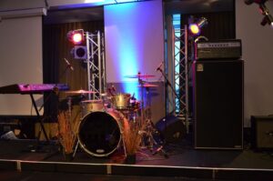 A drumkit and backline equipment set up on a stage, with uplighting in the background. Auckland Event hire production services.